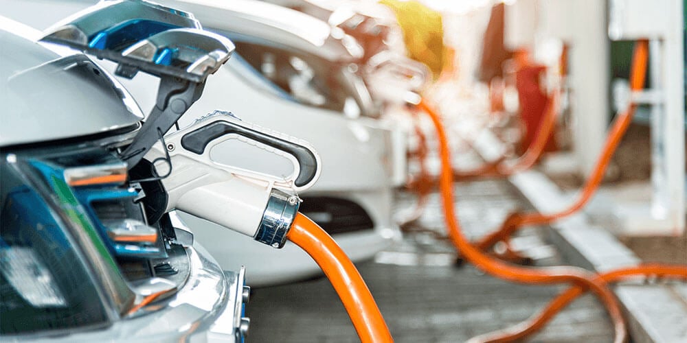 White electric vehicle parked at a workplace using a white and orange EV charging station  