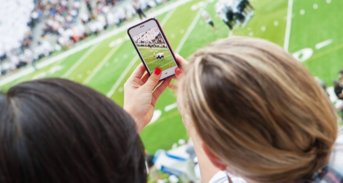 Two females using a phone inside a stadium.  